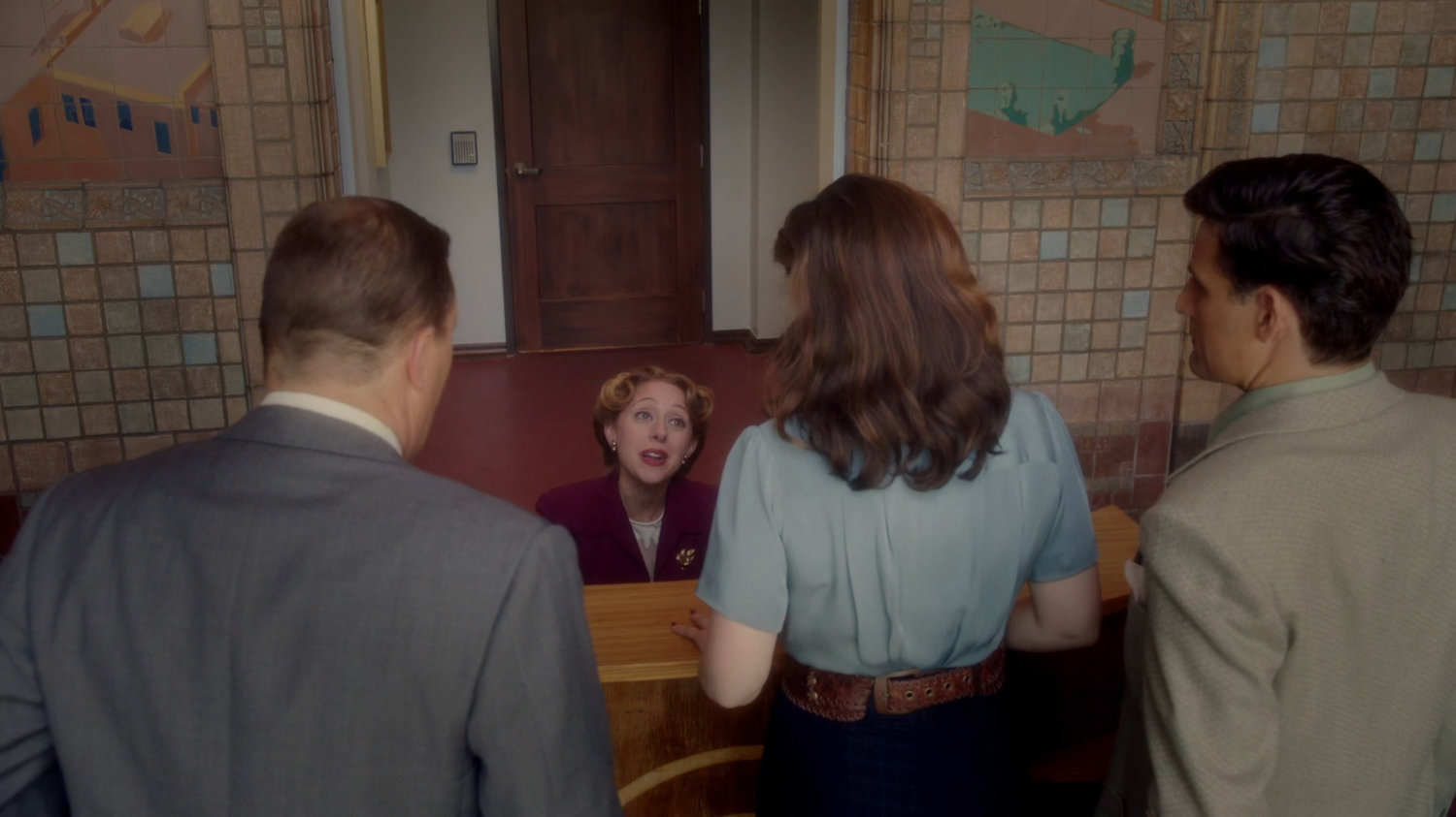 Sousa, Peggy, and Detective Henry speaking to receptionist in the Isodyne Energy lobby.