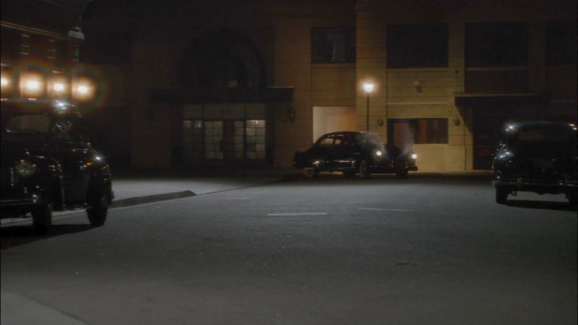 Car turning city street corner at night.