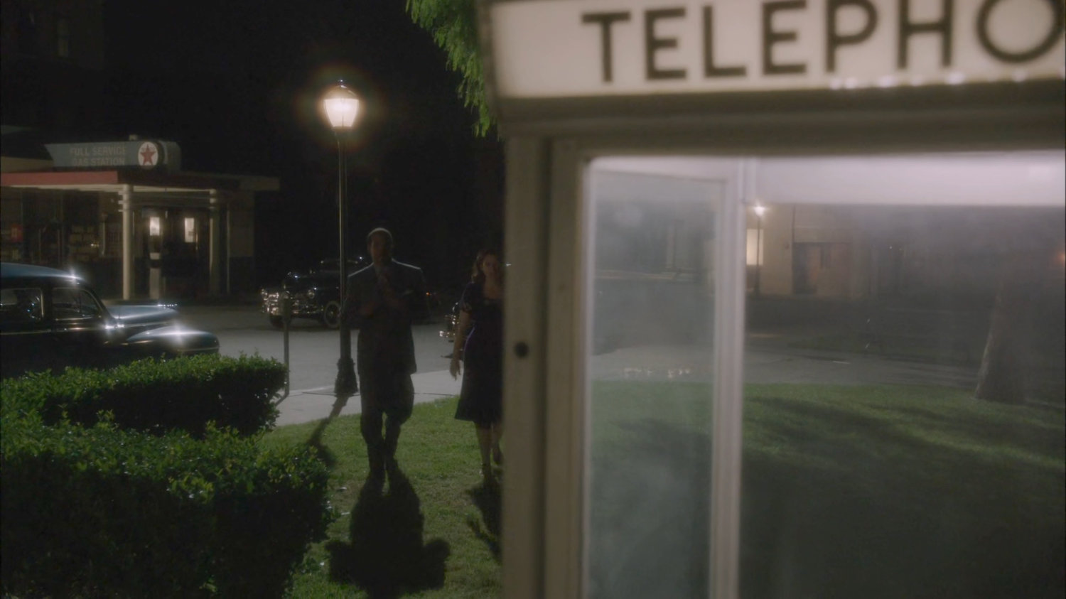 Jason and Peggy walk towards phone booth at night.