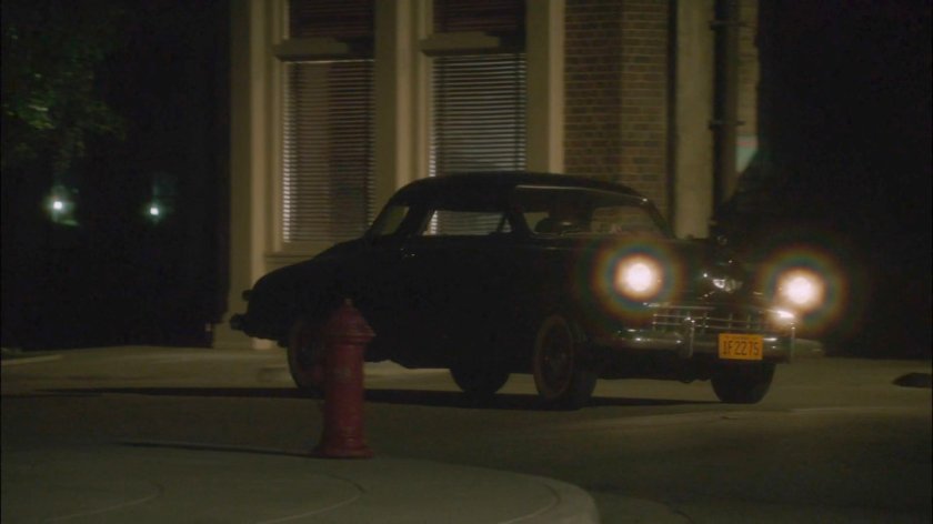 Car turning city street corner at night.