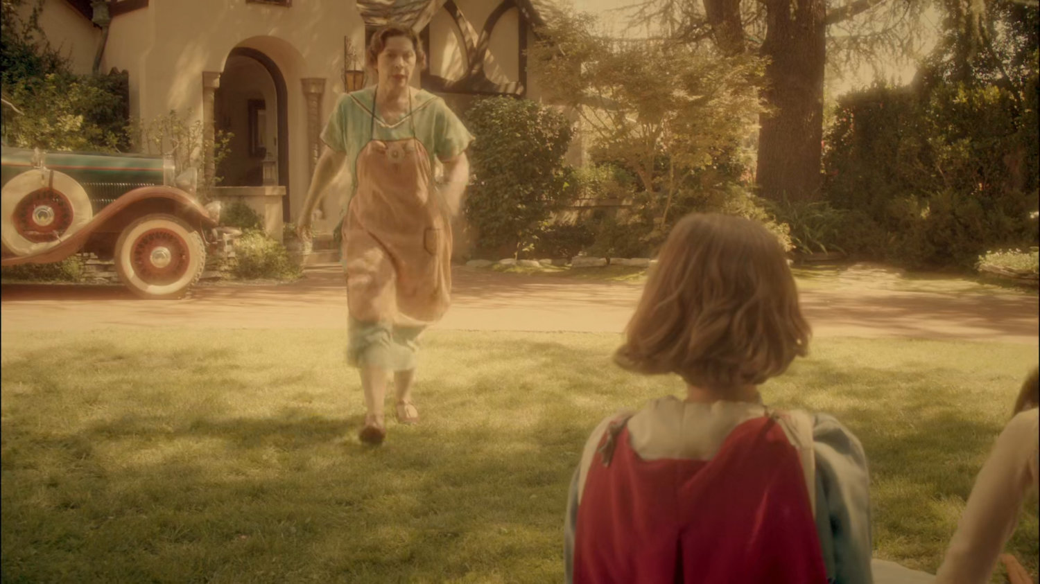 Young Peggy's mother walking towards her in their yard.