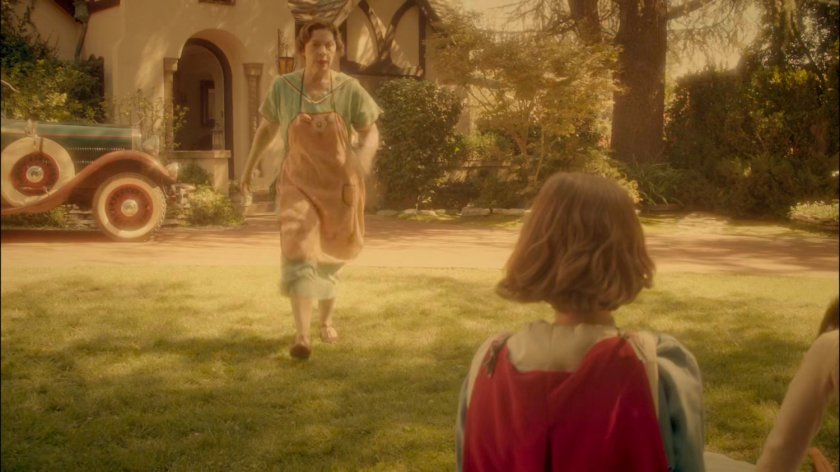 Young Peggy's mother walking towards her in their yard.