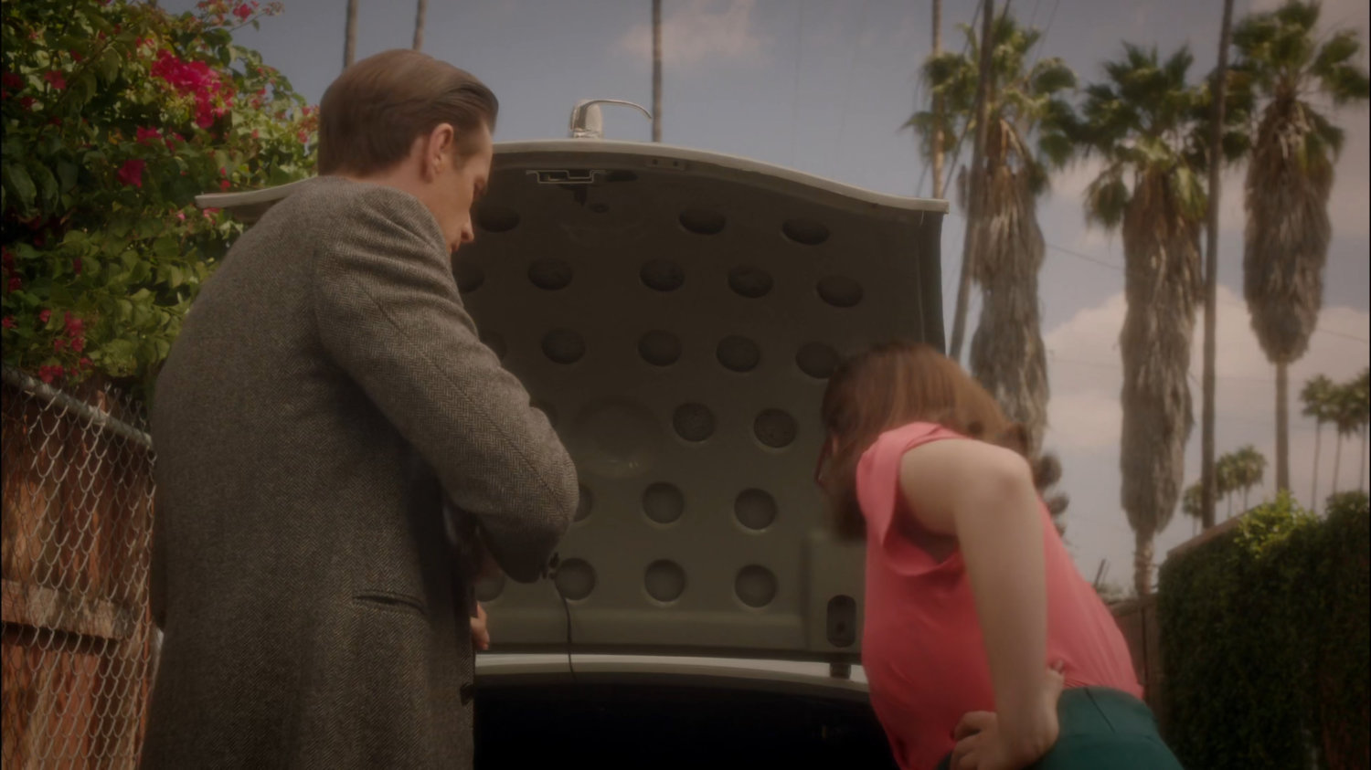 Peggy and Jarvis looking into trunk of car in a residential alley.