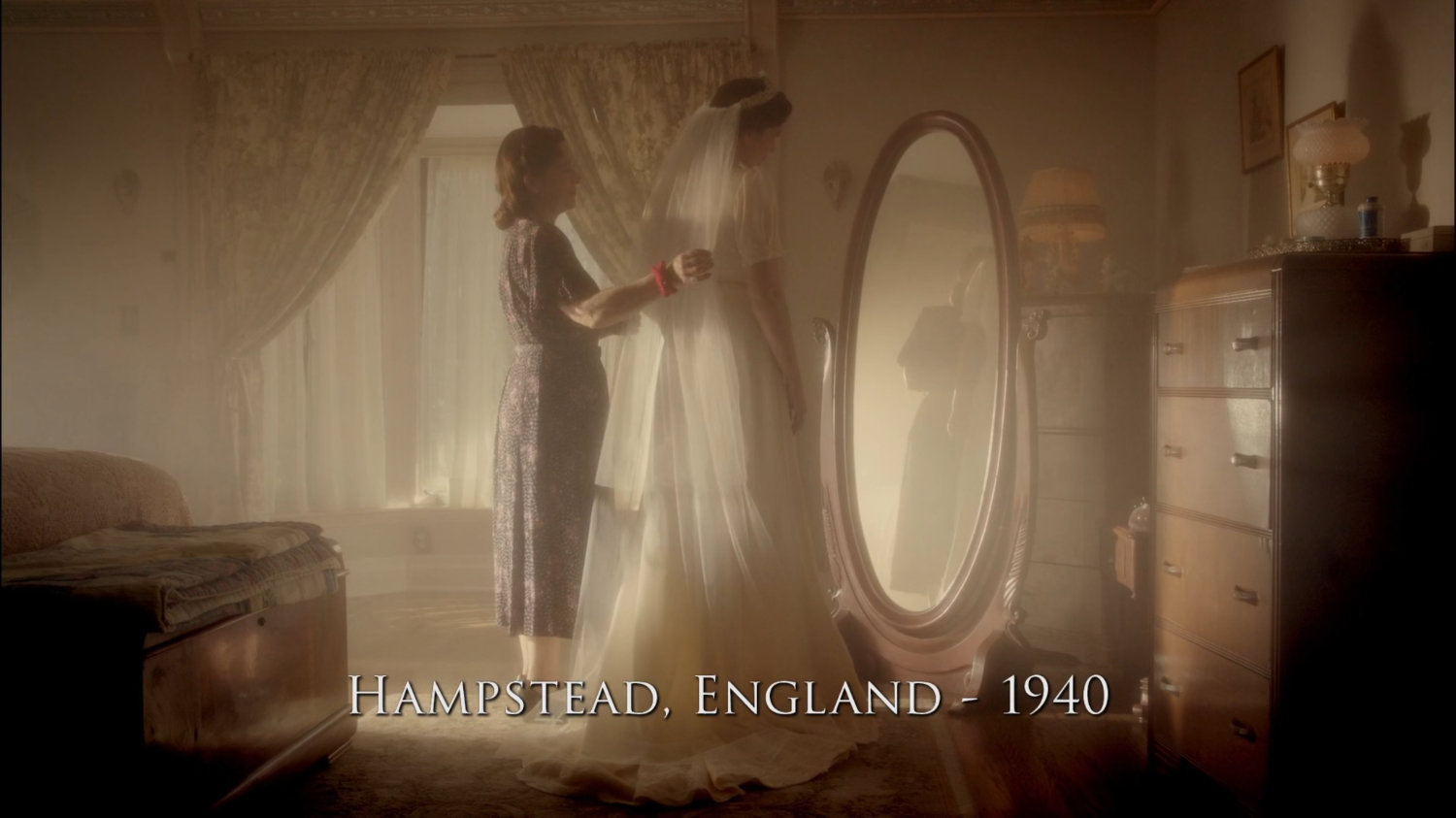 Peggy trying on her wedding dress with her mother at their house. Text: Hampstead, England - 1940.