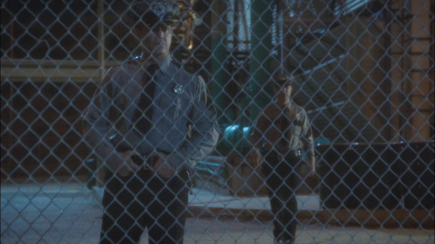 Security guards at Roxxon warehouse behind chain link fence.