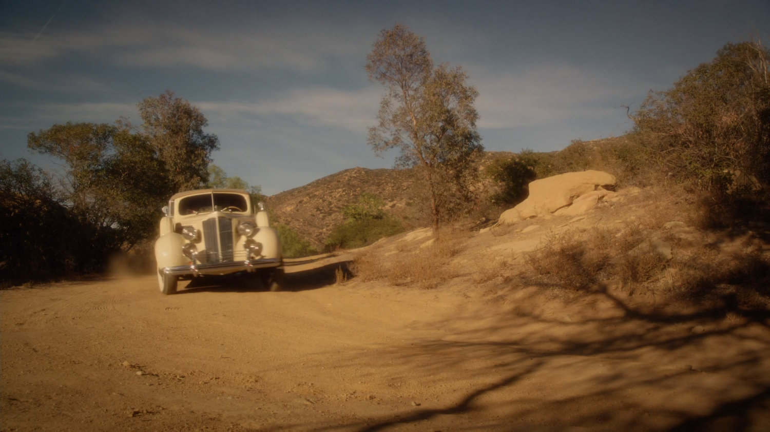 Car driving along dirt road in scrub hills.