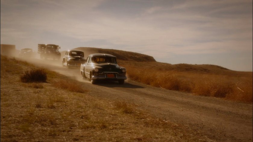 Vehicle convoy on dusty road in Mojave desert.