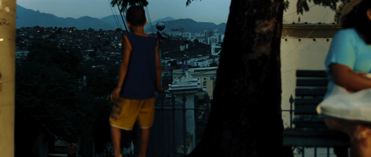 A young boy looks out over a slopped street and mountains in Mexico.