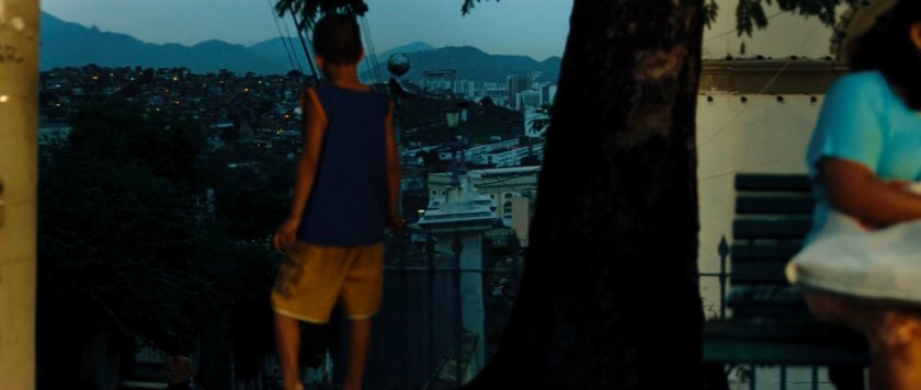 A young boy looks out over a slopped street and mountains in Mexico.
