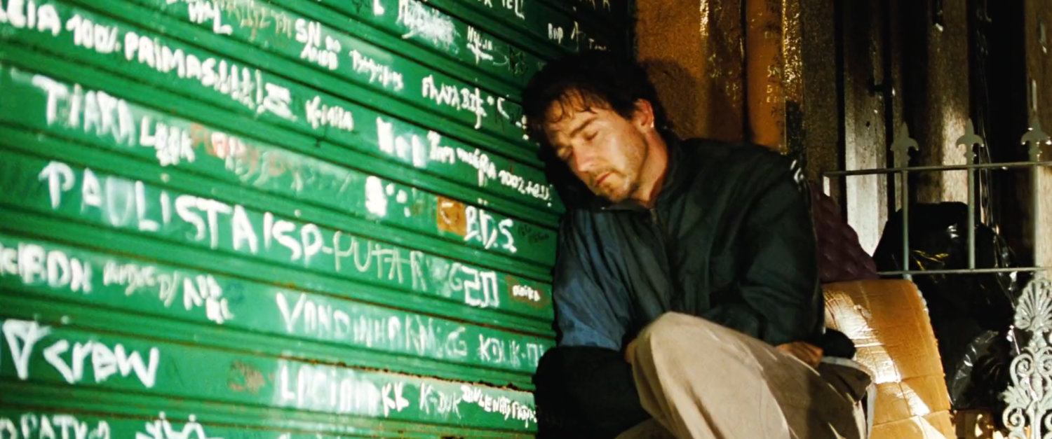 Bruce leans against a rollup door in Mexico covered with graffiti.