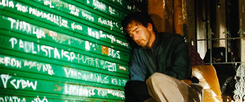 Bruce leans against a rollup door in Mexico covered with graffiti.