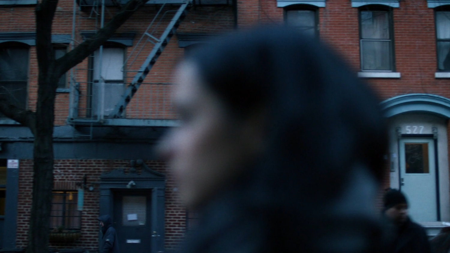 Jessica walking along a sidewalk, a building visible behind her.