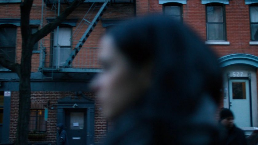 Jessica walking along a sidewalk, a building visible behind her.