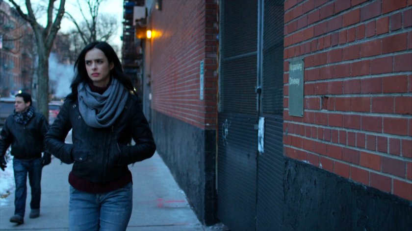 Jessica walking along a sidewalk towards a corner.