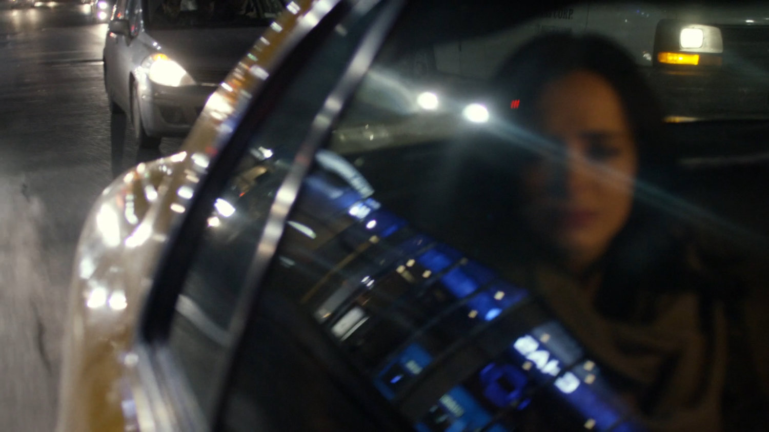 Jessica in the back seat of a taxi at night with reflections of stores in window.
