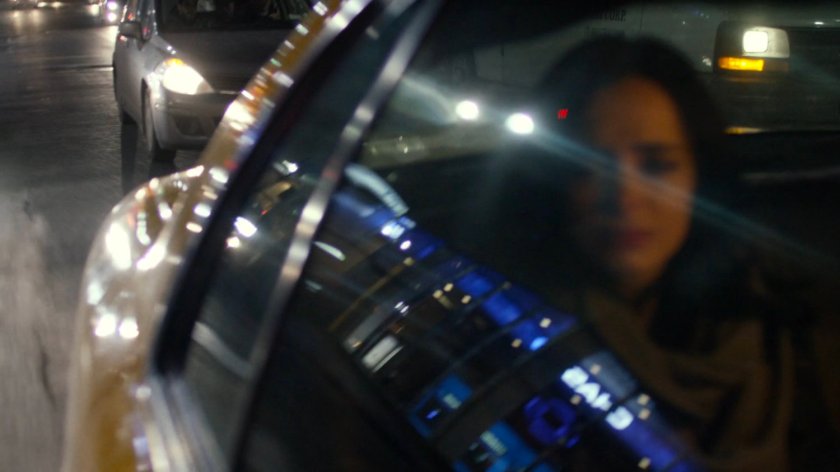 Jessica in the back seat of a taxi at night with reflections of stores in window.