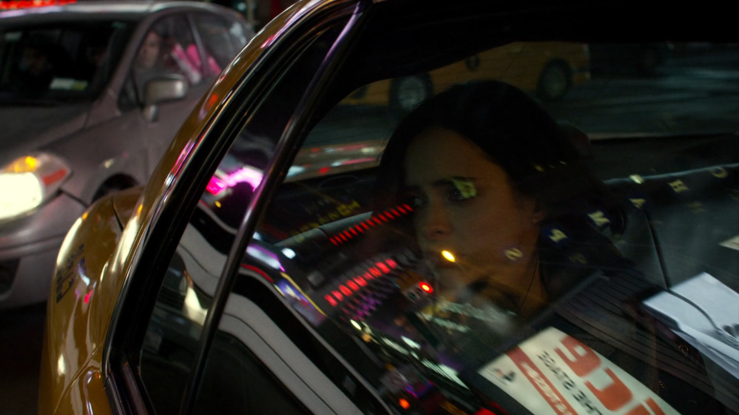 Jessica in the back seat of a taxi at night with reflections of stores in window.