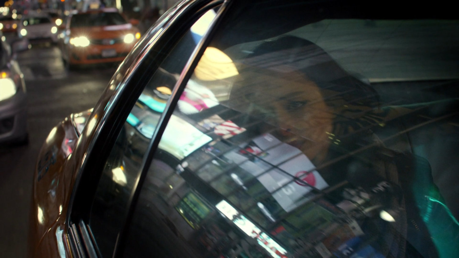 Jessica in the back seat of a taxi at night with reflections of stores in window.