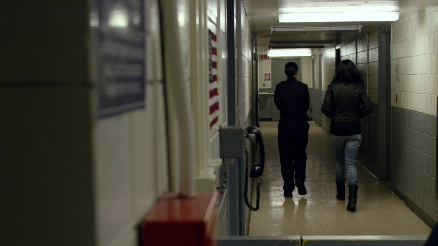 Jessica and guard in correctional facility hallway.