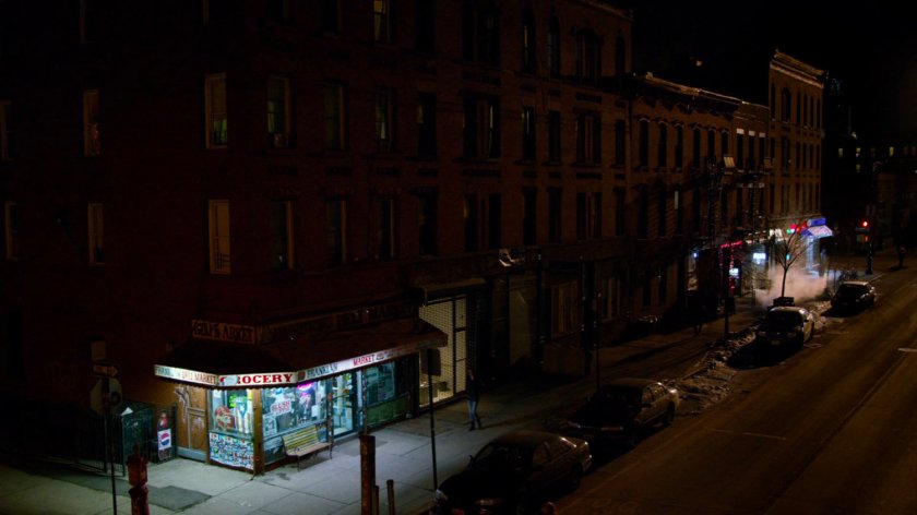 Jessica walking along a sidewalk towards corner store at night.