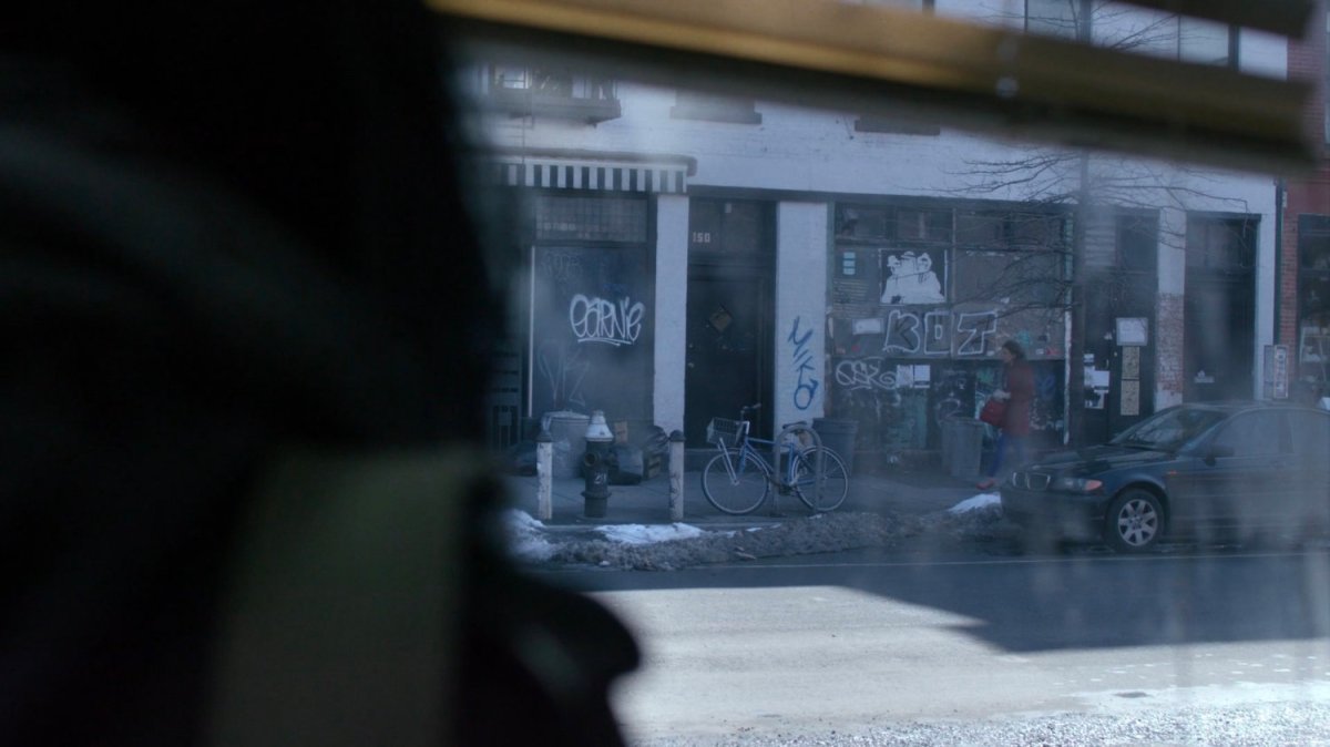 Jessica looking out window at graffiti on wall with Audrey Eastman walking by.
