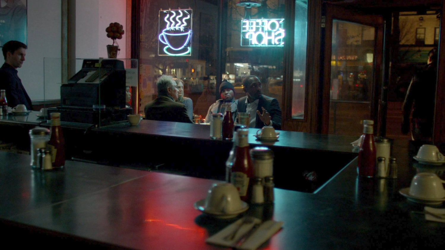 A support meeting of Kilgrave victims inside a diner.