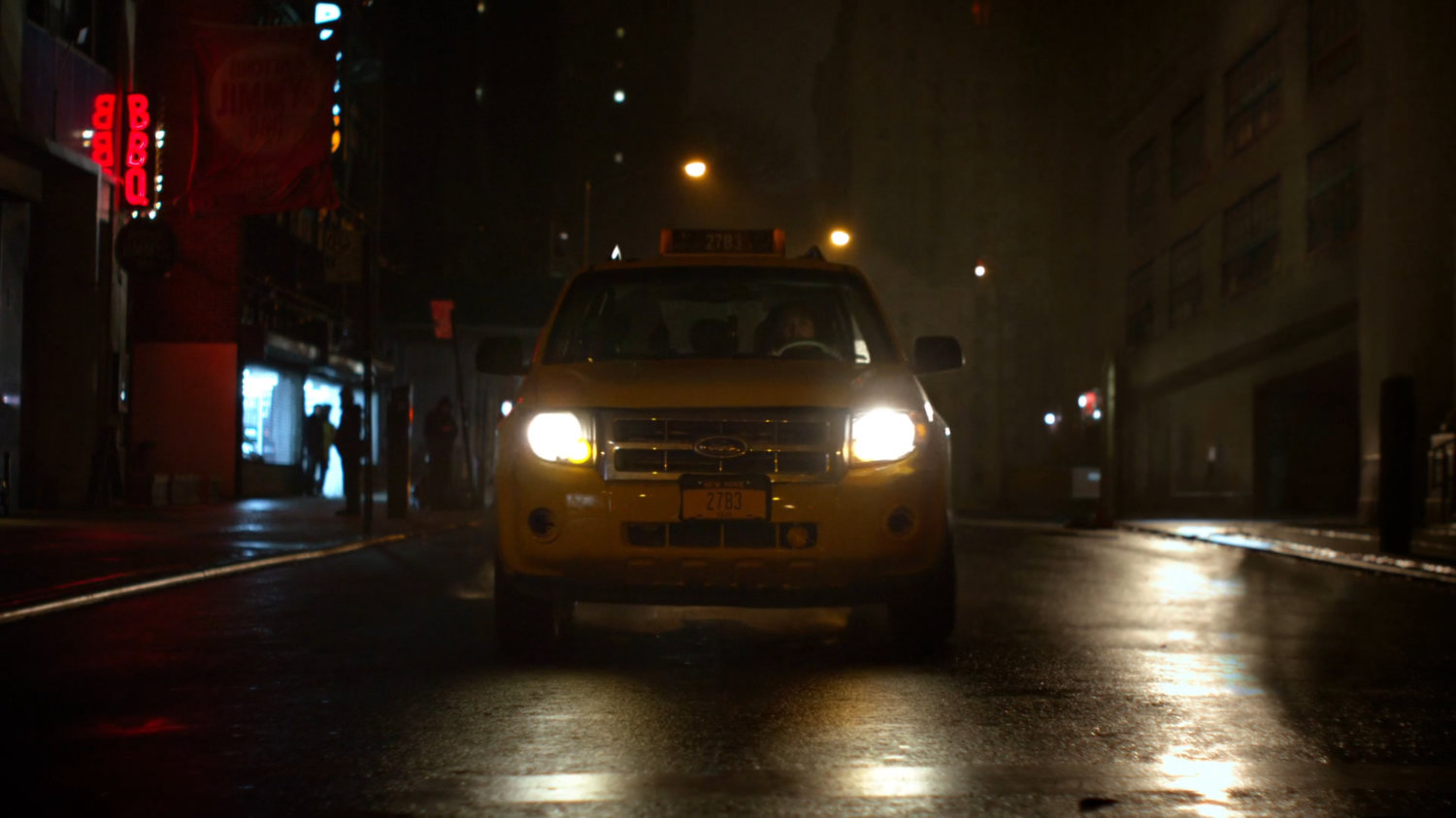A taxi driving along a street towards camera at night.