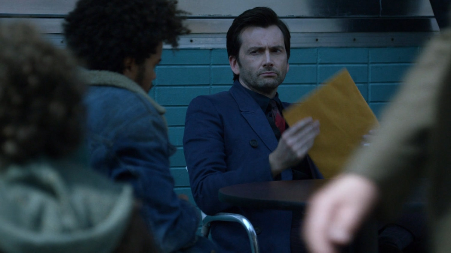 Kilgrave taking an envelope from Malcolm outside a coffee shop.