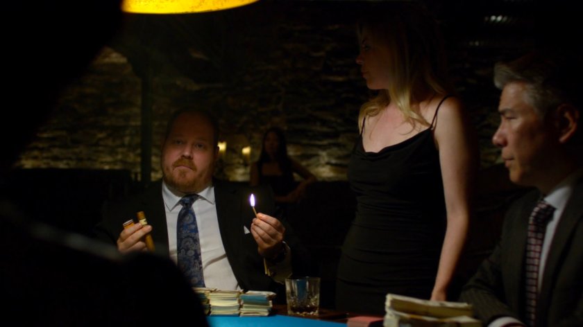 Poker player Harvey lighting a cigar at a poker table.