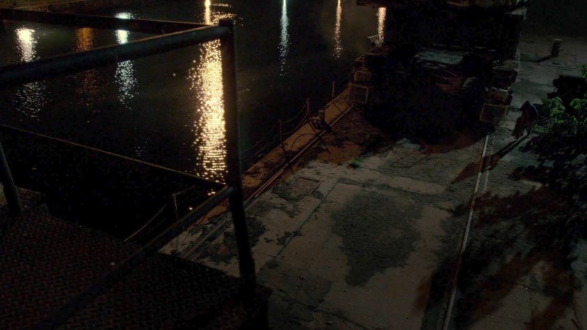 Malcolm dragging a body towards a dock at night.