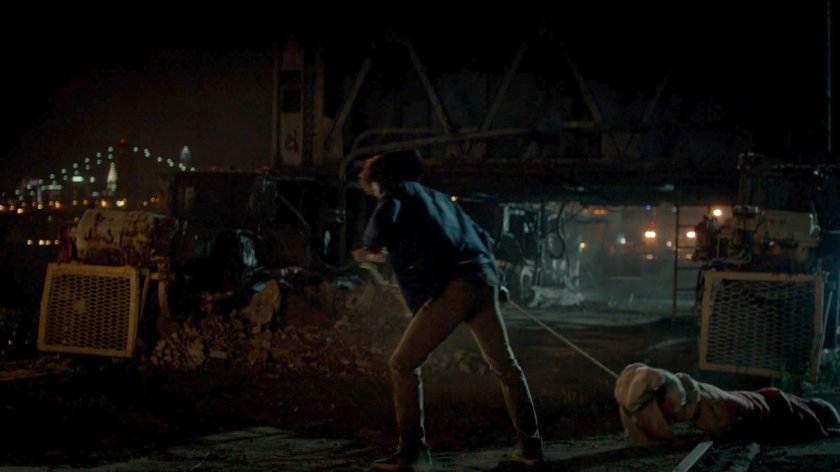 Malcolm dragging a body towards a dock at night.