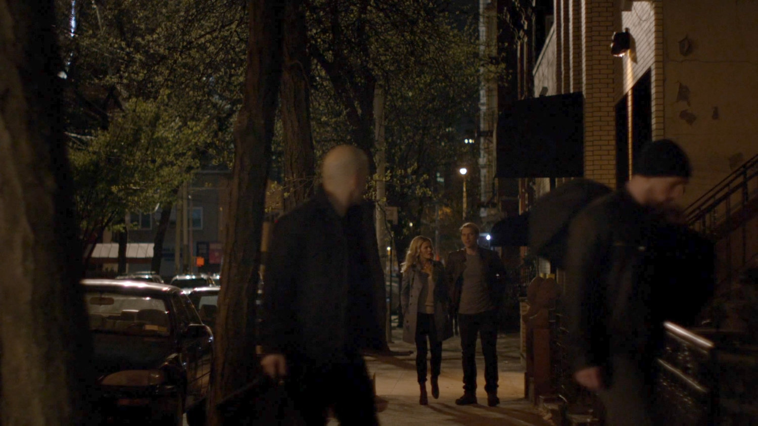 Simpson and Trish walk along a sidewalk at night.