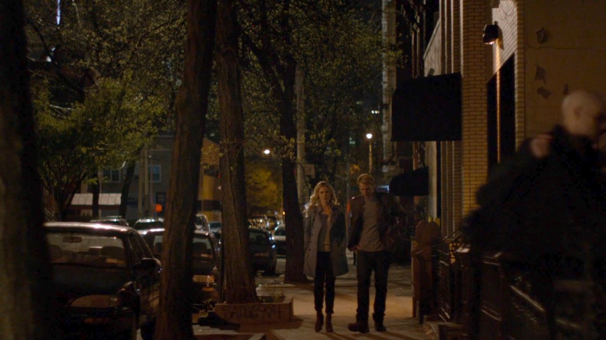Simpson and Trish walk along a sidewalk at night.
