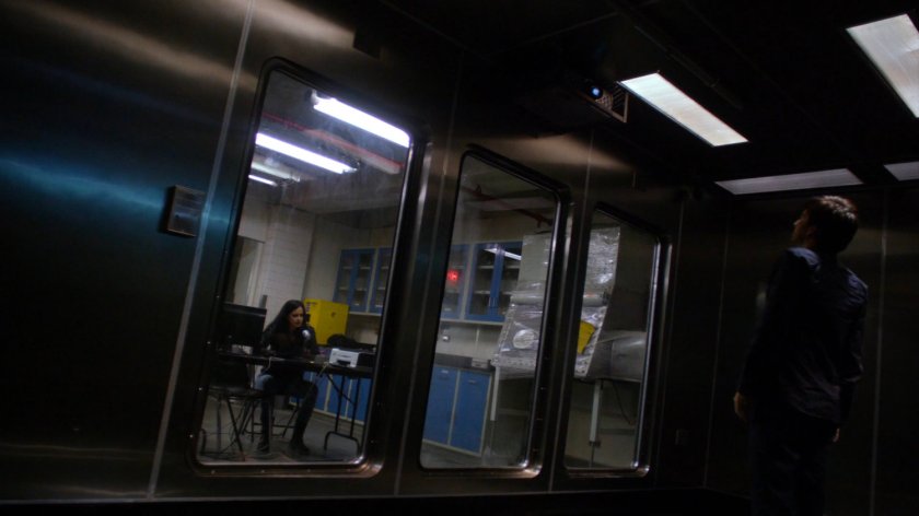 Jessica at a table looking into hermetically sealed room with Kilgrave at the CDC Facility.