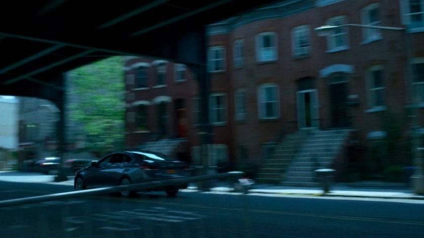 Trish's car speeding through city streets under overpass.