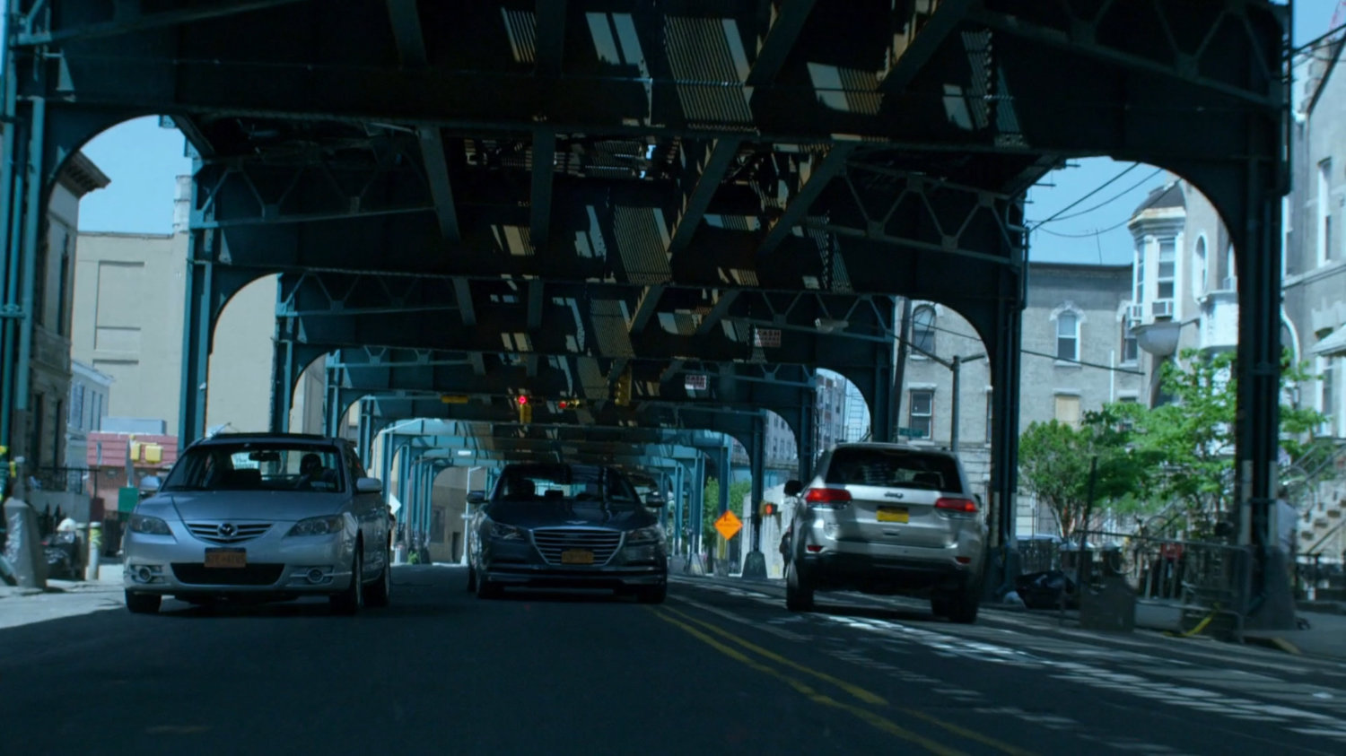 Trish's car speeding through city streets under overpass.