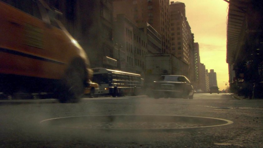 Cars driving along New York street at sunrise next to steaming manhole.
