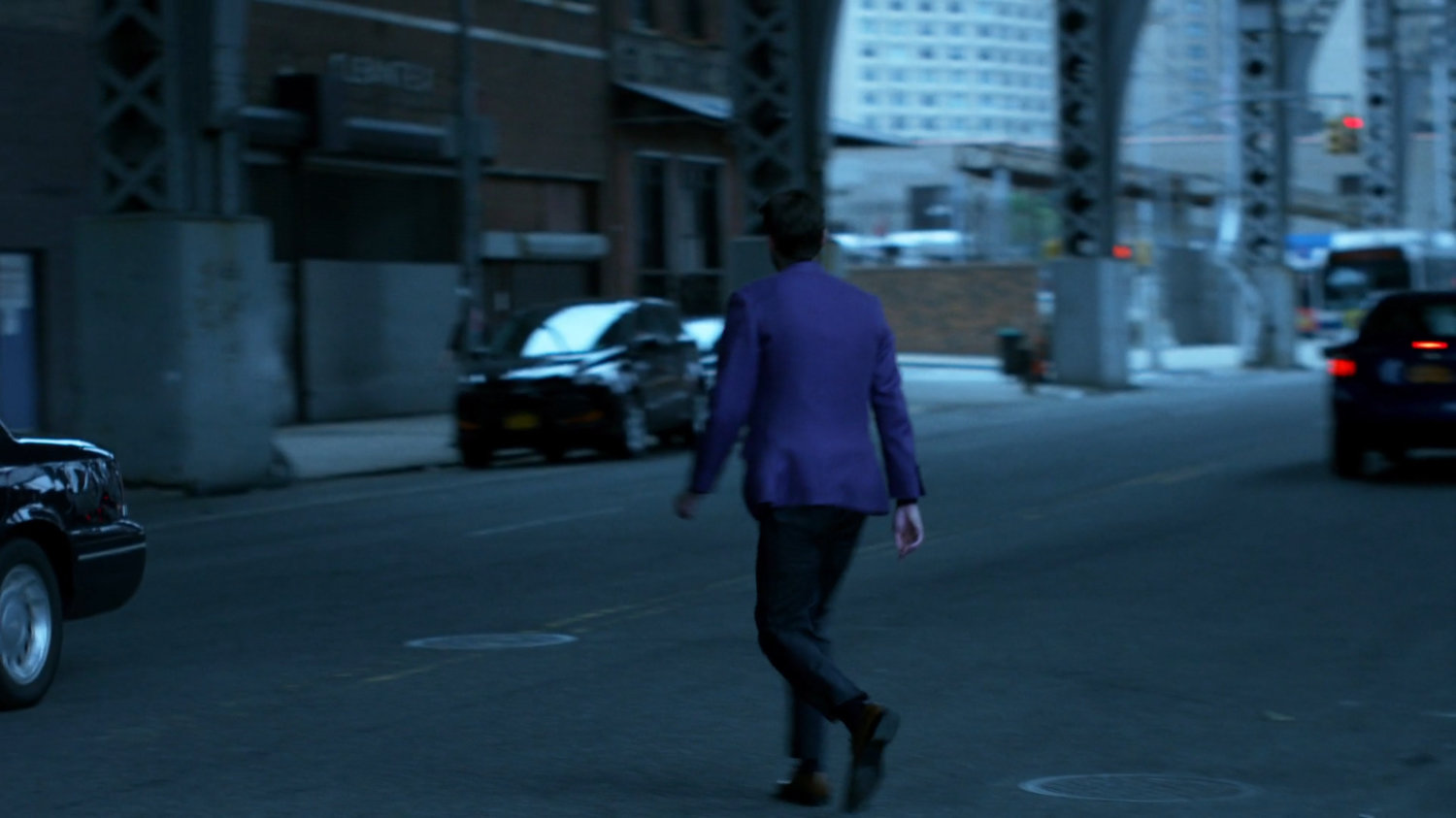Man in purple suit crossing street under overpass.
