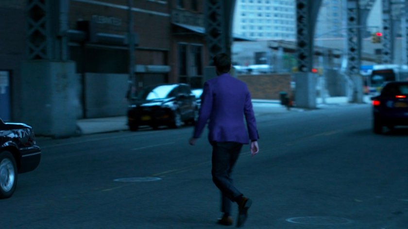 Man in purple suit crossing street under overpass.