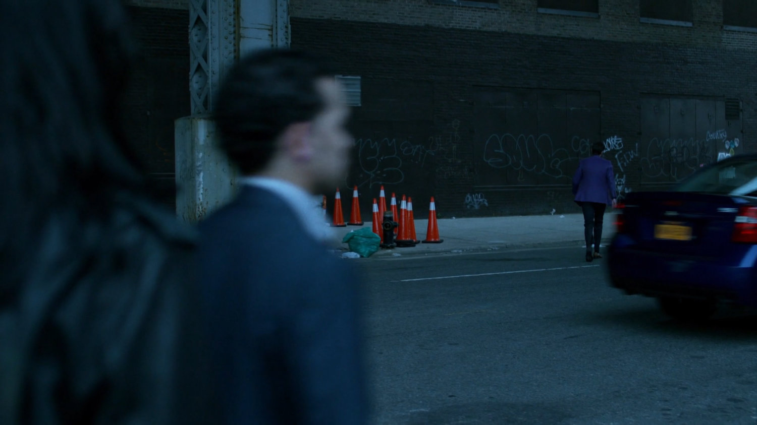Man in purple suit walking towards sidewalk under overpass.