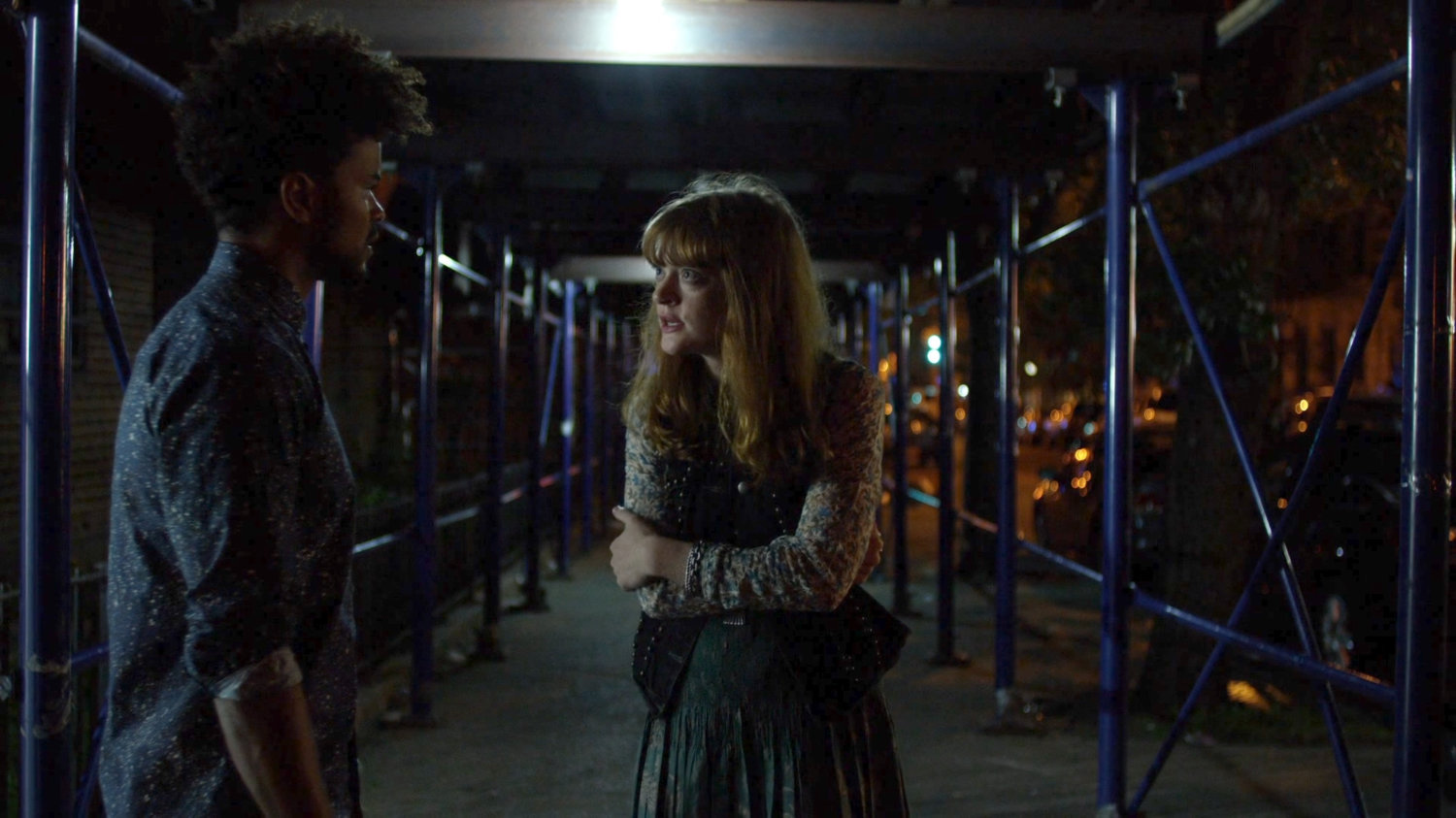 Malcolm and Robyn meeting on sidewalk under construction scaffolding at night.
