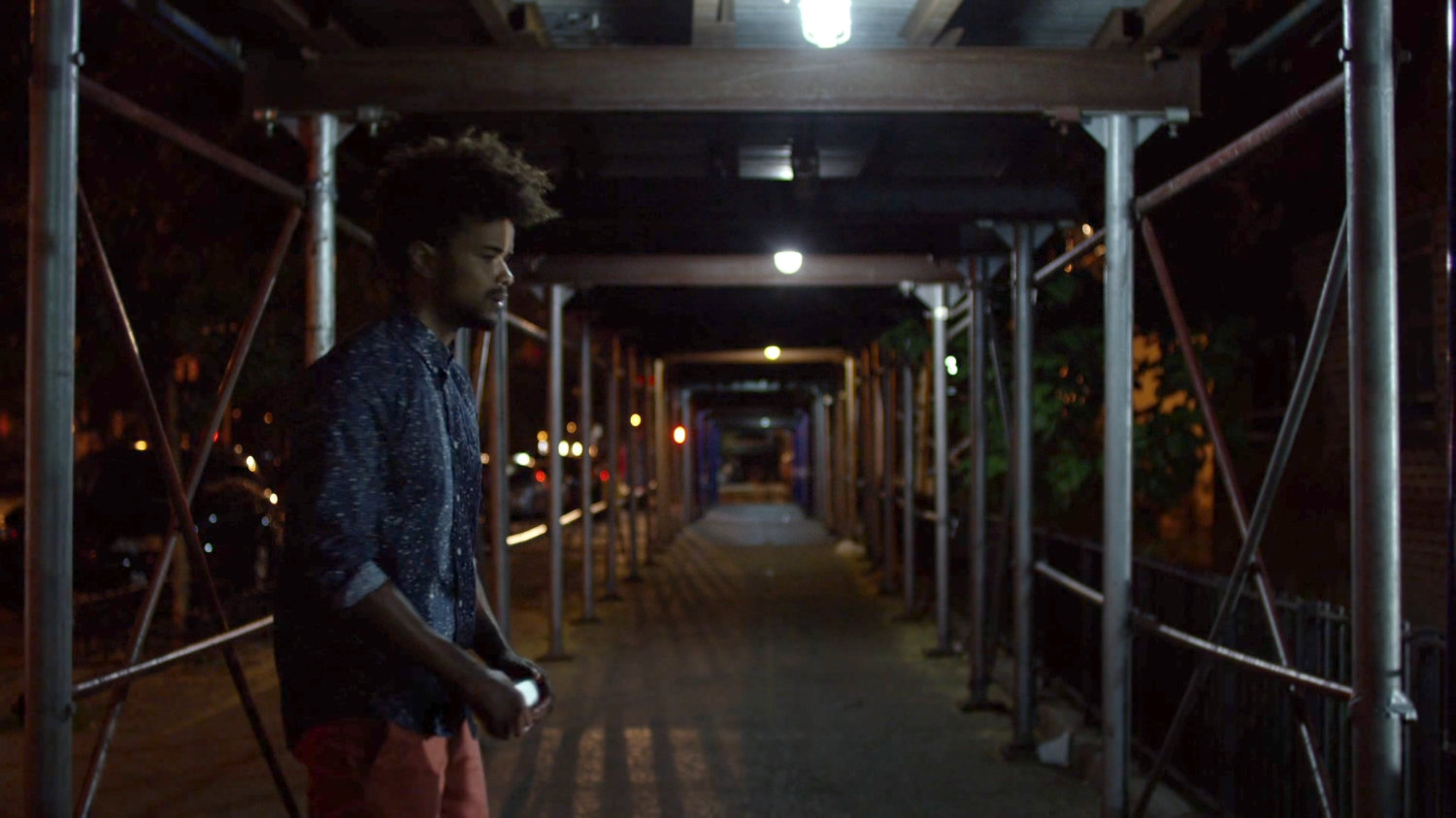 Malcolm on sidewalk under construction scaffolding at night.