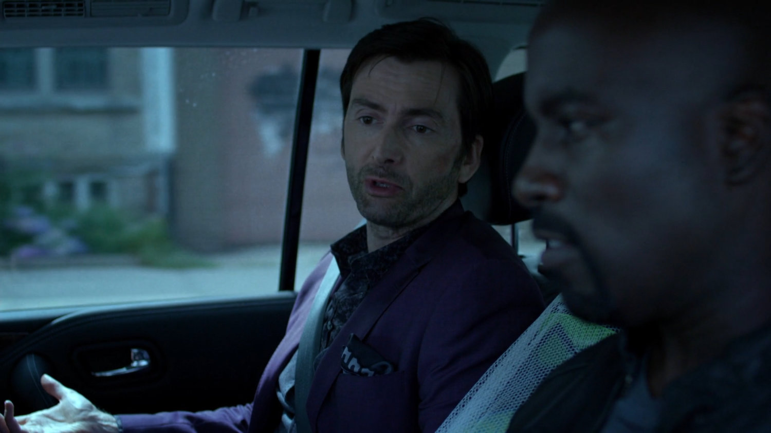 Luke and Kilgrave on back seat of car.