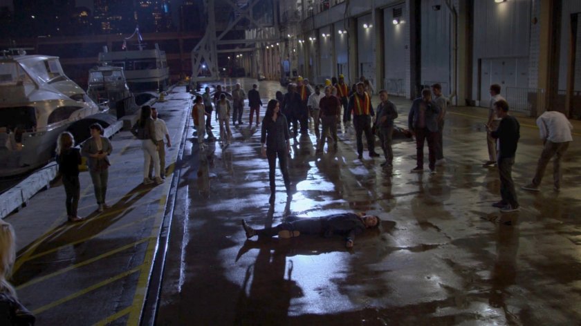 Jessica standing over the body of Kilgrave while civilians mill around behind her outside the Hudson Ferry Terminal.