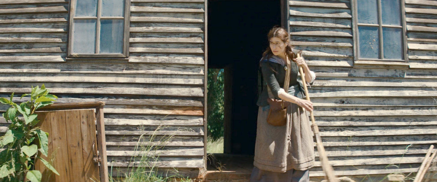 Agatha sweeps off porch outside wooden cabin, 1756.