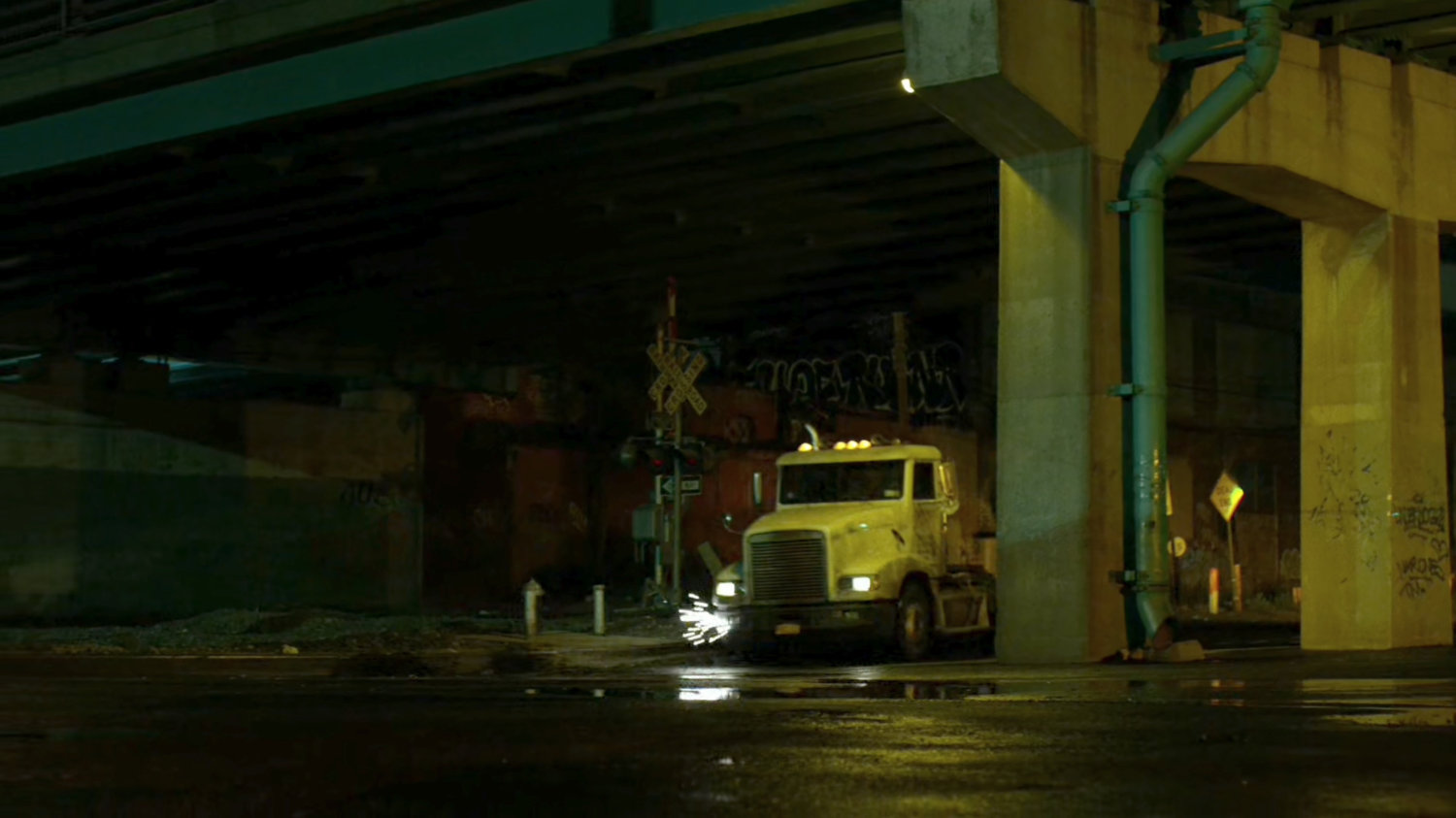 Truck drives under bridge at night.