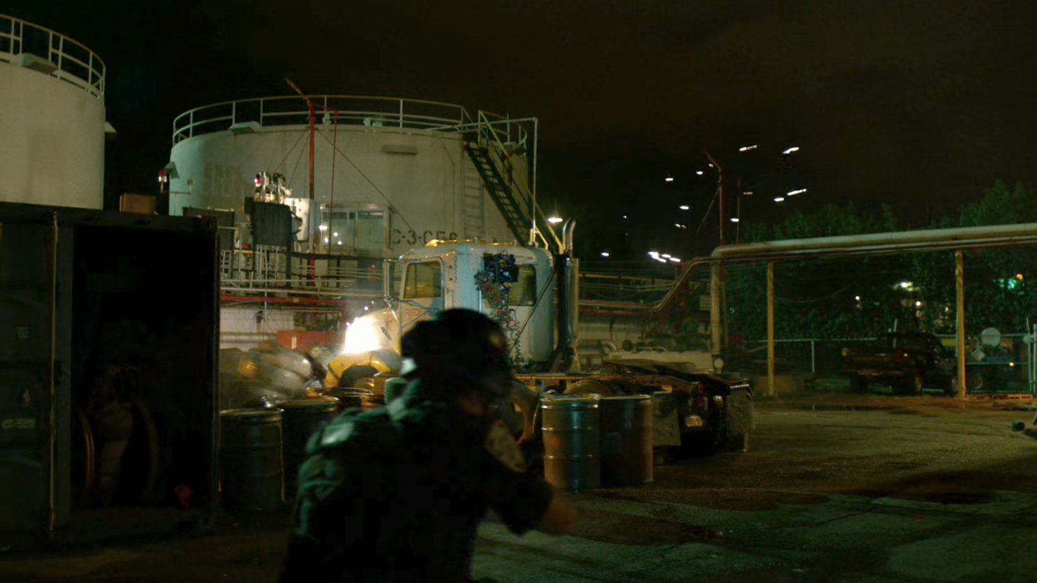 Police shoot semi trailer outside refinery at night.
