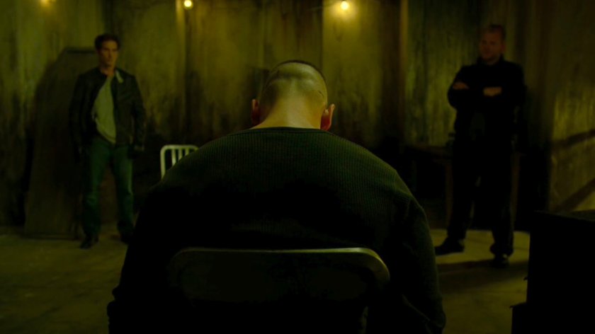 Frank tied to a chair in catacombs flanked by two Irish mobsters.