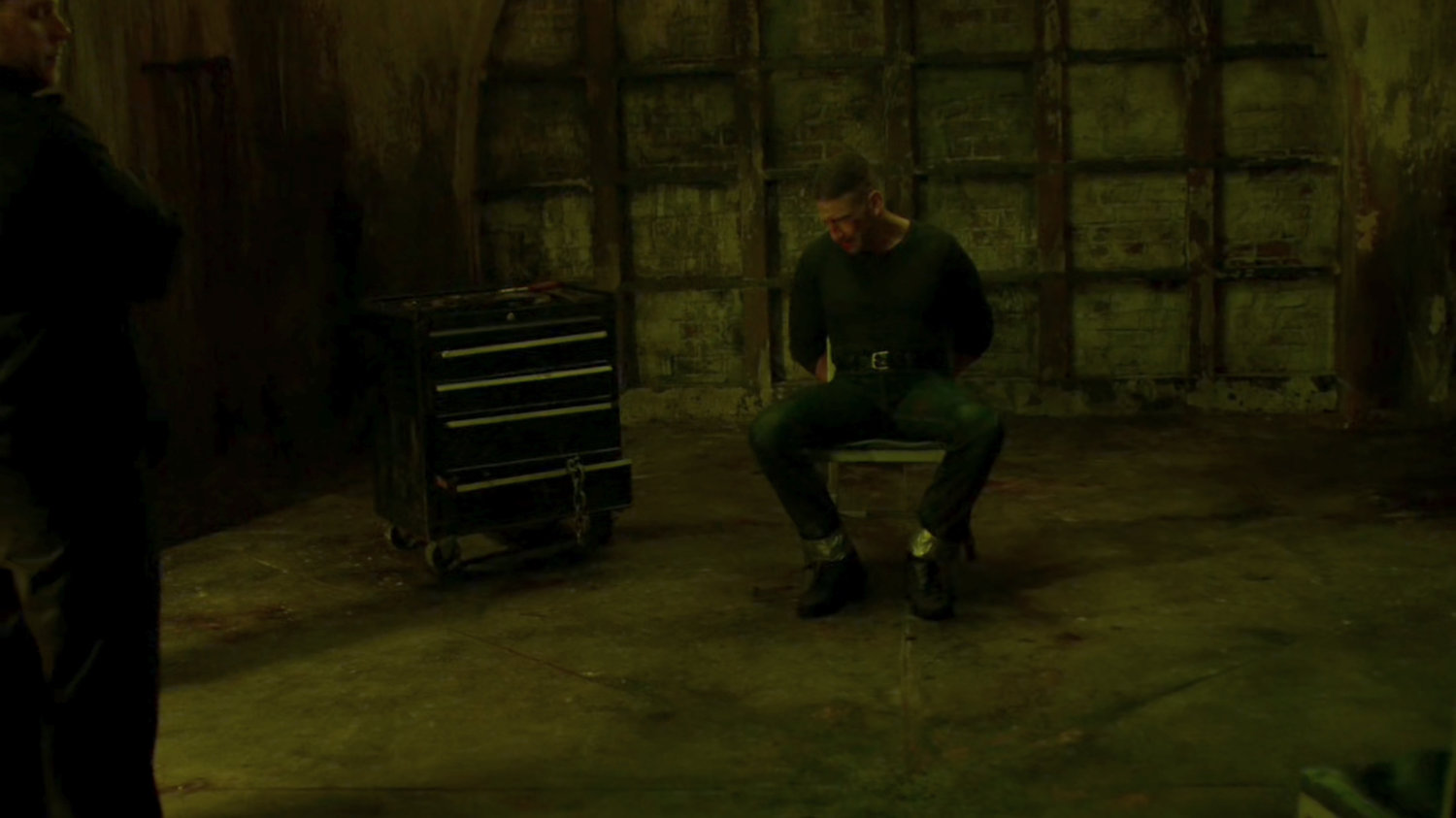 Frank tied to a chair in catacombs.