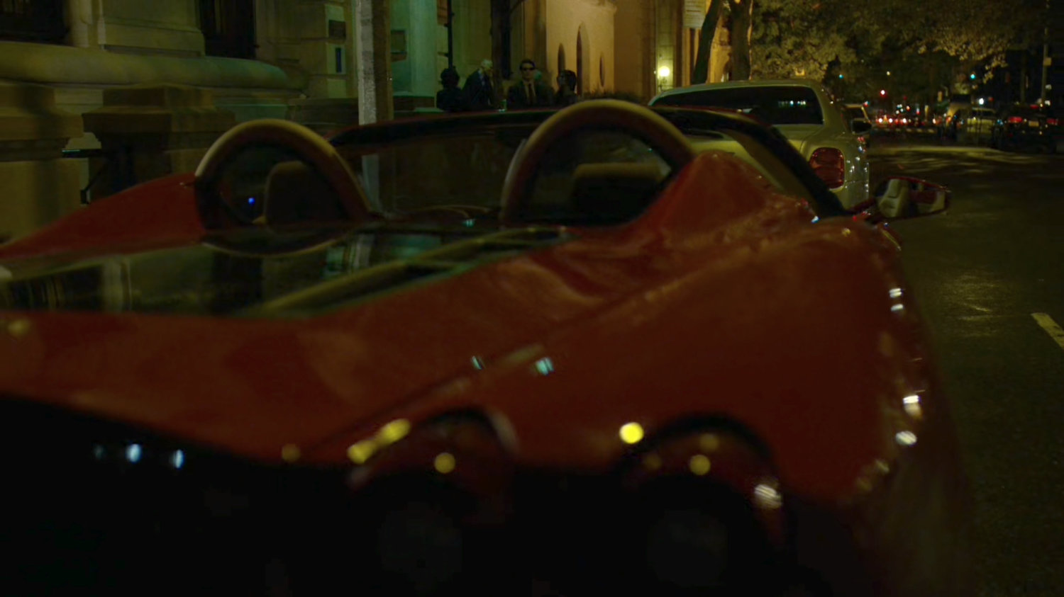 A red sports car parked on the street outside faculty party.